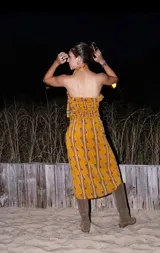 Vestido midi strapless color dorado con estampado de hojas y rayas verticales. Incluye una tira de tela que se ata al cuello.