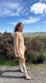 Vestido corto color beige, con escote en V con cordones, mangas 3/4 acampanadas con cordones, hombros descubiertos y corte holgado.