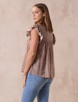 Blusa color marrón claro de algodón con bordados y calados blancos. Tiene cuello a la base, escote en V con lazo de ajuste y mangas cortas amplias.