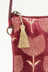 Bolso pequeño tipo cartera porta celular, confeccionado en terciopelo color borgoña con diseño bordado de tulipanes dorados. Tiene acceso superior con cierre y tirante en hilo metalizado, más cordón largo que permite colgarlo al cuerpo.
