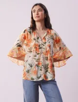 Blusa de gasa estampada con flores color naranja, marca Figueroa & Flower. Tiene cuello a la base, escote en V con lazo, abertura central con botones, delantera plisada y mangas 3/4 amplias.