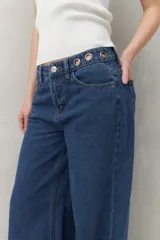Pantalón de jean negro de corte ultra wide, tiro medio y detalles metálicos en la cintura.