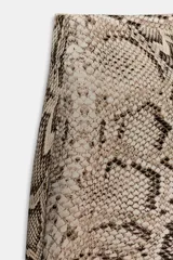 Pantalón de tiro alto con estampado de piel de serpiente en tonos beige y marrón. Tiene bolsillos laterales ocultos en la costura y falsos bolsillos de vivo en la espalda. El cierre frontal es con cremallera y ganchos metálicos.