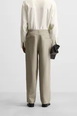 Pantalón negro de corte amplio, con pliegues frontales, bolsillos laterales y traseros de ojal. Incluye cinturón de la misma tela con hebilla metálica.