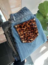 Pantalón de jean azul con bolsillos traseros desmontables con estampado animal print. Los bolsillos se sujetan al pantalón con remaches metálicos.
