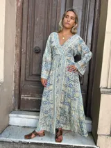 Vestido largo fluido con escote en V y mangas abullonadas 3/4. Presenta un estampado tipo paisley en tonos celeste, beige y gris.