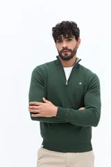 Sweater de tejido liso color verde oscuro, con cuello medio y cierre frontal parcial plateado. Presenta puños y cintura acanalados, y un pequeño logo bordado en el pecho.