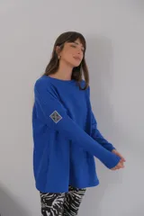 Buzo azul de viscosa con cuello redondo y manga larga. Presenta un aplique con diseño geométrico en el brazo izquierdo.