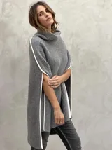 Poncho tejido de punto grueso color gris con cuello alto y aberturas laterales con ribete blanco.