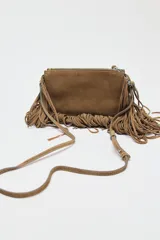 Bandolera marrón de serraje con flecos largos en la parte inferior. Tiene asa de hombro y bandolera extraíbles, doble bolsillo interior y cierre con cremallera.