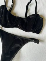 Conjunto de terciopelo negro, compuesto por un corpiño con aros, breteles regulables y detalle de puntilla en el escote, y una tanga con elásticos regulables a los costados.