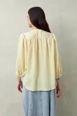 Camisa celeste a rayas verticales, de corte amplio y mangas 3/4. Presenta cuello mao, cierre frontal con botones irregulares y detalle de pespuntes y pinzas en el canesú.