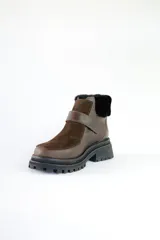 Bota corta de cuero color marrón con puntera y empeine de gamuza color beige. Tiene cuello de piel sintética color crema, cierre con velcro y suela track.