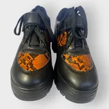 Zapatillas negras con detalles en animal print naranja y cordones negros.