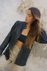 Camisa negra de cuero ovino con cuello mao, cierre frontal con botones a presión, dos bolsillos de parche en el pecho y tachas doradas en cuello, bolsillos y mangas.