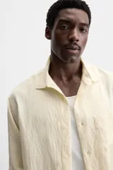 Camisa color crema de corte relaxed fit, confeccionada en tejido con mezcla de viscosa. Tiene cuello solapa, manga larga con puños abotonados, bolsillo de parche en el pecho y cierre frontal con botones.