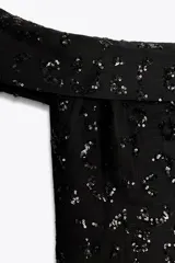 Top chaleco negro con escote recto y hombros descubiertos, con lentejuelas a tono y aberturas laterales.