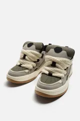 Zapatilla deportiva estilo skate color gris y verde, con cordones anchos color crema, lengüeta acolchada, tirador trasero y suela gruesa de goma color caramelo.