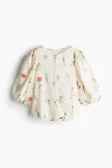 Blusa de lino color blanco con estampado de flores, cuello redondo, cierre de botones y mangas globo tres cuartos con puños elásticos.