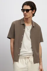Camisa marrón de punto con textura, corte regular, cuello inglés, tapeta lisa, canesú en la espalda, bajo recto con aberturas laterales y manga corta.