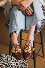 Zapato blucher de cuero con estampado animal print en tonos marrones y dorados, con cordones finos color borgoña y detalle de flor en el extremo del cordón.