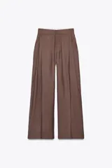 Pantalón marrón de tiro alto con trabillas, doble pliegue, bolsillos laterales y tapetas en la espalda. Pierna ancha y cierre frontal con cremallera y gancho metálico.