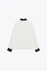 Camisa blanca de manga larga con cuello y puños negros. Cierre frontal con botones.