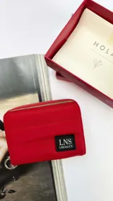 Billetera corta con cierre alrededor y tapa, confeccionada en tela capitoneada. Incluye varias reparticiones con tarjeteros y bolsillos internos, y una correa de mano desmontable. Disponible en negro, rojo y dorado.
