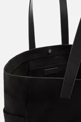 Bolso tipo shopper negro fabricado en tejido de algodón con asas de piel. Cuenta con dos bolsillos laterales exteriores y un bolsillo interno.