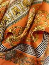 Pañuelo cuadrado de satén color naranja con estampado de motivos florales y grecas en tonos dorados, marrones y beige.
