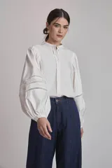 Camisa blanca de mangas largas abullonadas con detalles de calado en los puños, cuello mao y cierre frontal con botones.