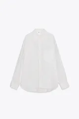Camisa blanca con finas rayas verticales negras, de corte holgado, cuello solapa, manga larga con puños y bolsillo de plastrón en el pecho.