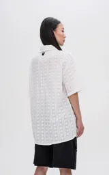 Camisa blanca con textura y botones marrones, de corte holgado y mangas cortas.