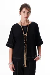 Blusa negra de lino con mangas 3/4 y cuello redondo. Presenta pespuntes a contratono en blanco en el cuello, puños y ruedo.