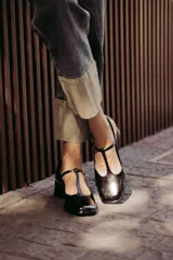 Zapatos de charol negro con diseño tipo T-bar, taco bajo cuadrado y punta redondeada.