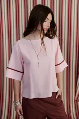Blusa holgada de lino color rosa pálido con escote redondo y mangas 3/4. Presenta un ribete de color marrón oscuro en el borde de las mangas.