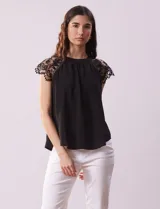 Blusa negra de crepe con apliques de crochet en los hombros. Tiene cuello redondo, mangas cortas y espalda con abertura ojal y botones.