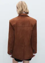 Chaqueta marrón de piel caprina con cuello de pico con solapa, diseño recto, cierre delantero con botones, forro interior, manga larga y dos bolsillos de solapa en la parte frontal.