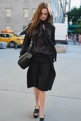 Blusa negra de cuello redondo con lazo en el mismo tejido. Manga larga acampanada y bajo recto.