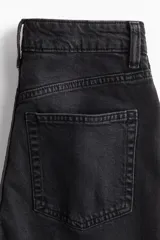 Pantalón de jean negro de corte ancho, largo tobillero y terminación desflecada. Con tiro alto, cinco bolsillos, cierre con cremallera y botón metálico.
