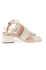 Sandalias de cuero color crema con tira entre los dedos, correa ajustable en el tobillo y tachas doradas.