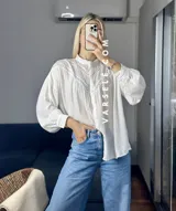 Camisa blanca de mangas largas con detalles de encaje en el cuello y en el frente.