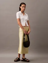 Cartera bandolera negra de cuero sintético con textura granulada, forma de media luna y correa fina ajustable. Cierre con solapa magnética y logo de Calvin Klein grabado en el frente.