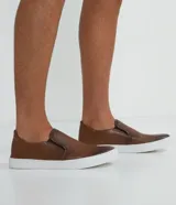 Championes slip on marrones de cuero, con talón flexible y suela blanca.