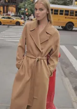 Abrigo largo color camel, con cuello con solapas, manga larga, cinturón desmontable y bolsillos laterales.