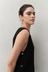 Blusa sin mangas negra de punto suave y fluido, con silueta larga y recta. Presenta botones dorados en los laterales.