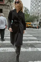 Gabardina larga color beige, con cuello solapa, manga larga con trabillas en hombros y cierre frontal cruzado con botones negros. Incluye cinturón a tono anudado.