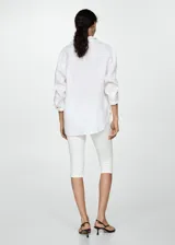 Camisa blanca de lino, de corte oversize, manga larga con puños abotonados, cuello camisero y cierre frontal con botones.