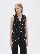 Chaleco largo sin mangas negro con estampado de lunares blancos, cuello en V y corte entallado.