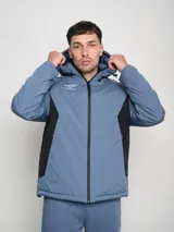 Campera corta de abrigo Umbro Crafted Pro, color negro con paneles laterales en gris. Presenta capucha con cordón ajustable, cierre frontal completo y logo de la marca bordado en el pecho.